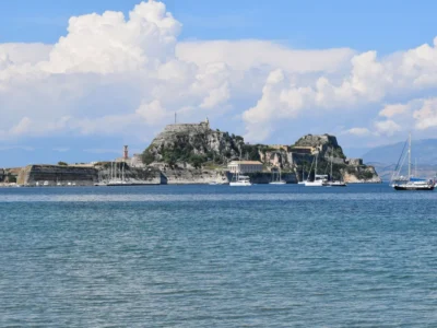 Oude Fort van Corfu-stad aan zee met zeilboten en stapelwolken