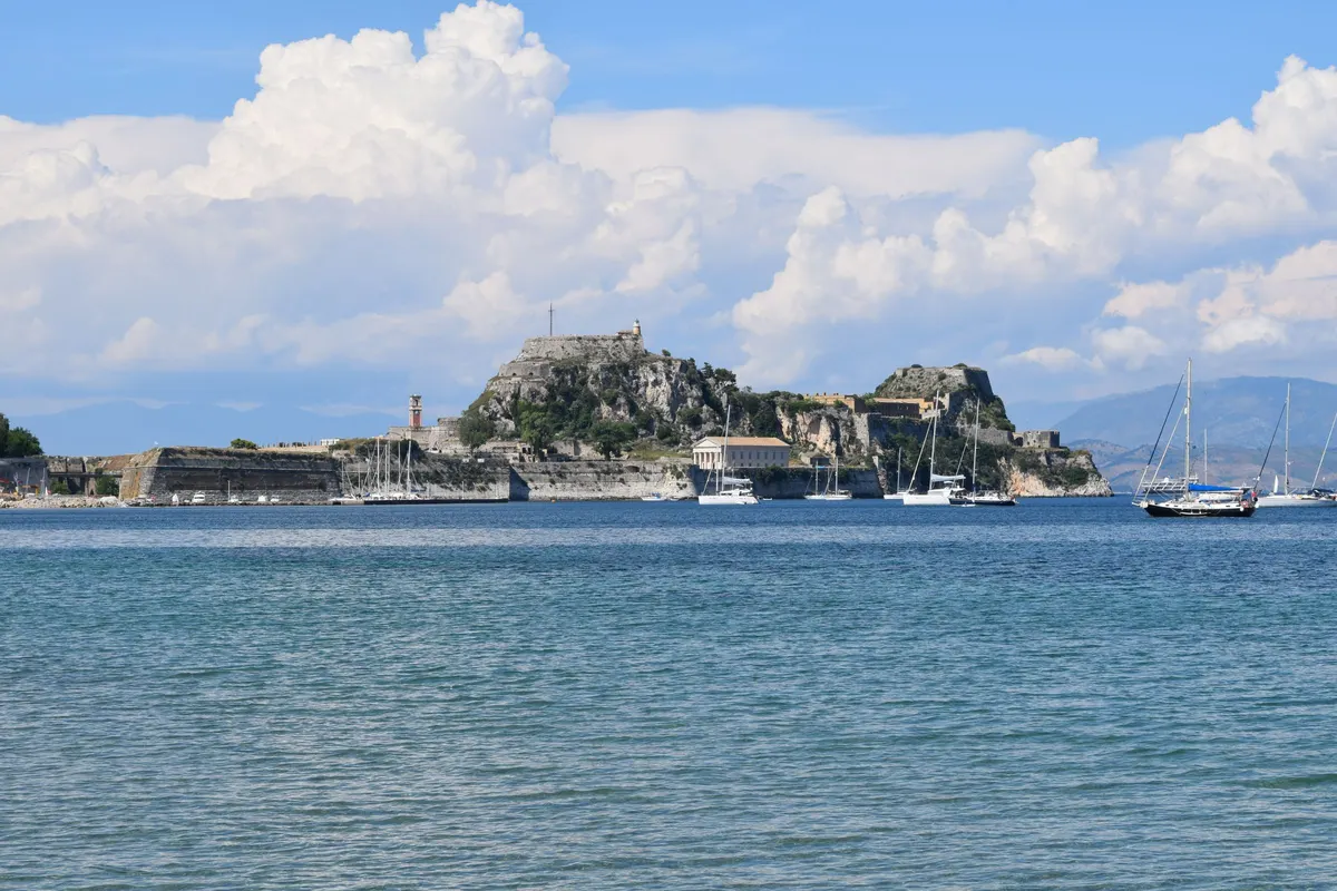 Oude Fort van Corfu-stad aan zee met zeilboten en stapelwolken