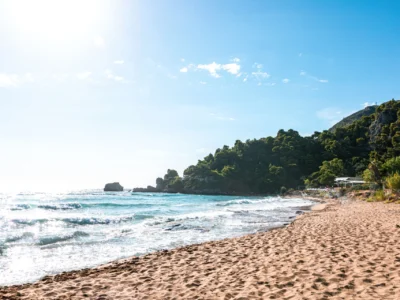 Zonnig strand met groene heuvels en helderblauw water op Corfu