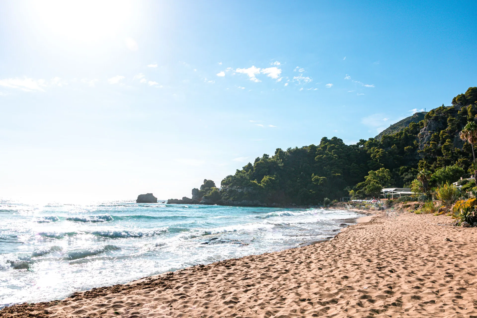 Zonnig strand met groene heuvels en helderblauw water op Corfu