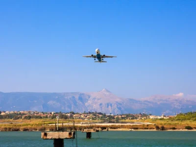 Vliegtuig in de landing boven het water bij het vliegveld van Corfu met bergen op de achtergrond