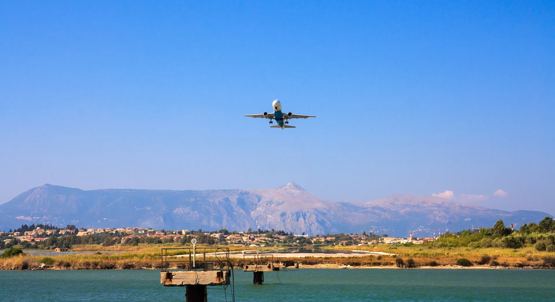 Vliegtuig in de landing boven het water bij het vliegveld van Corfu met bergen op de achtergrond