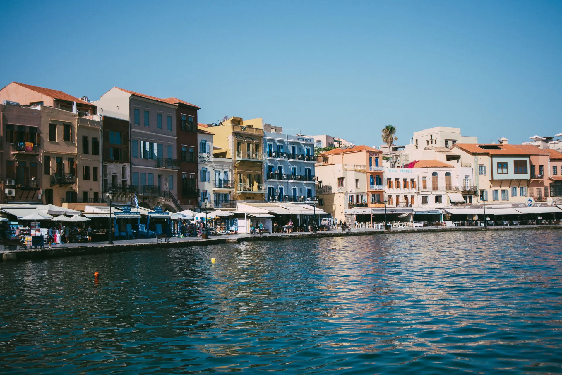 Kleurrijke gevels langs de Venetiaanse haven van Chania op Kreta onder een blauwe lucht