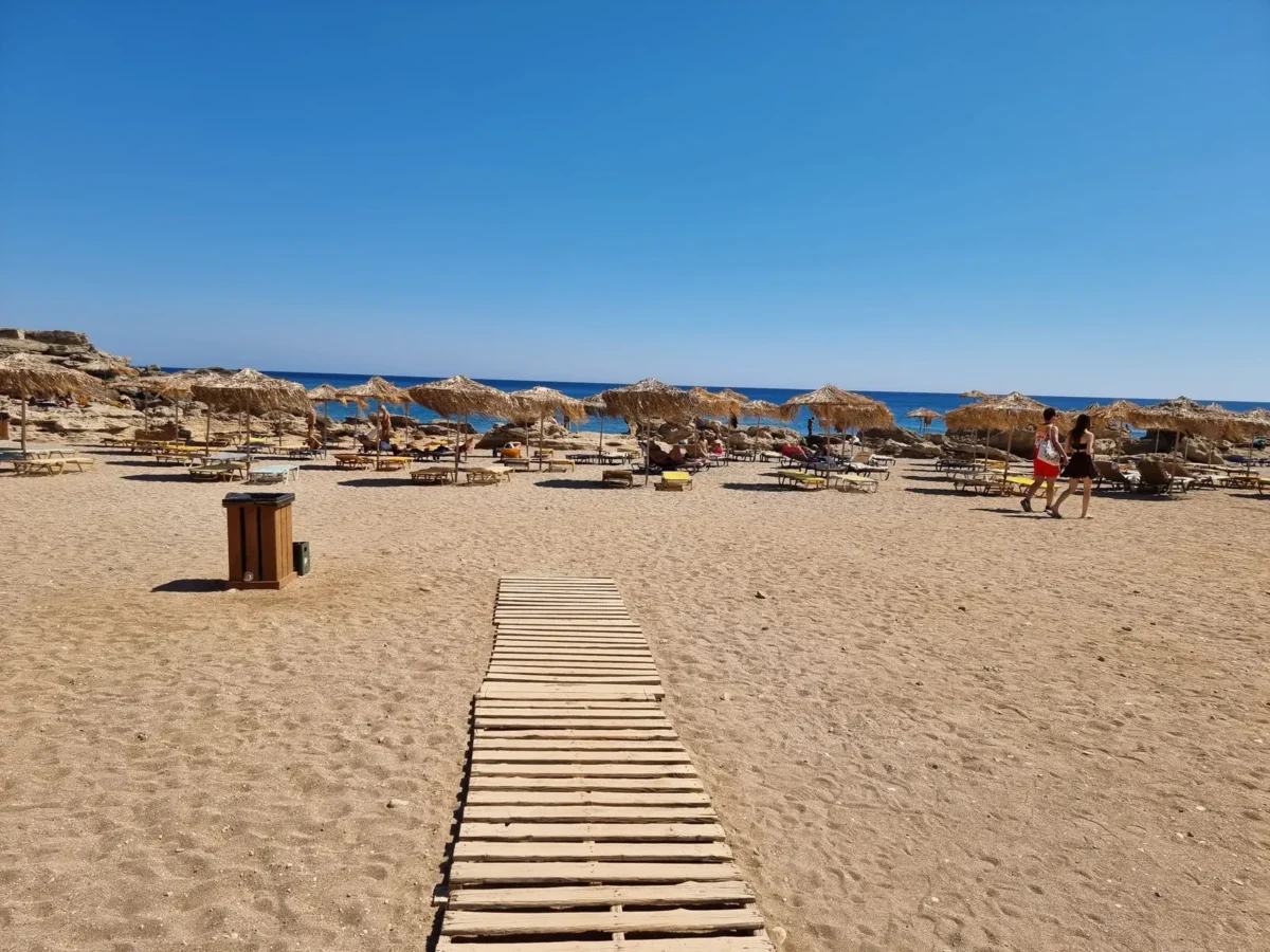 Zandstrand op Rhodos met een houten strandpad en parasols aan zee