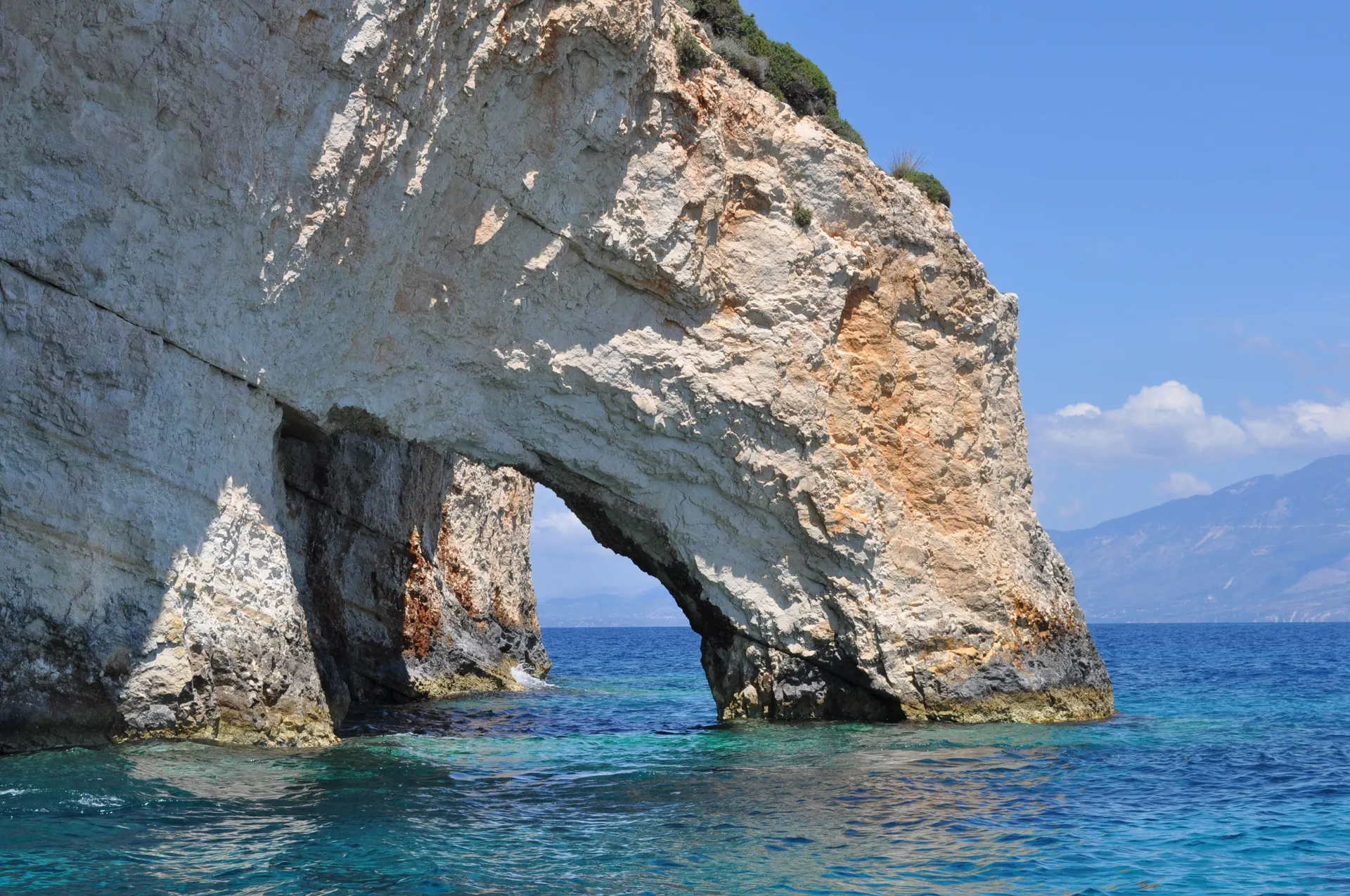 Kalkstenen rotsboog boven helderblauw water bij de Blauwe Grotten van Zakynthos